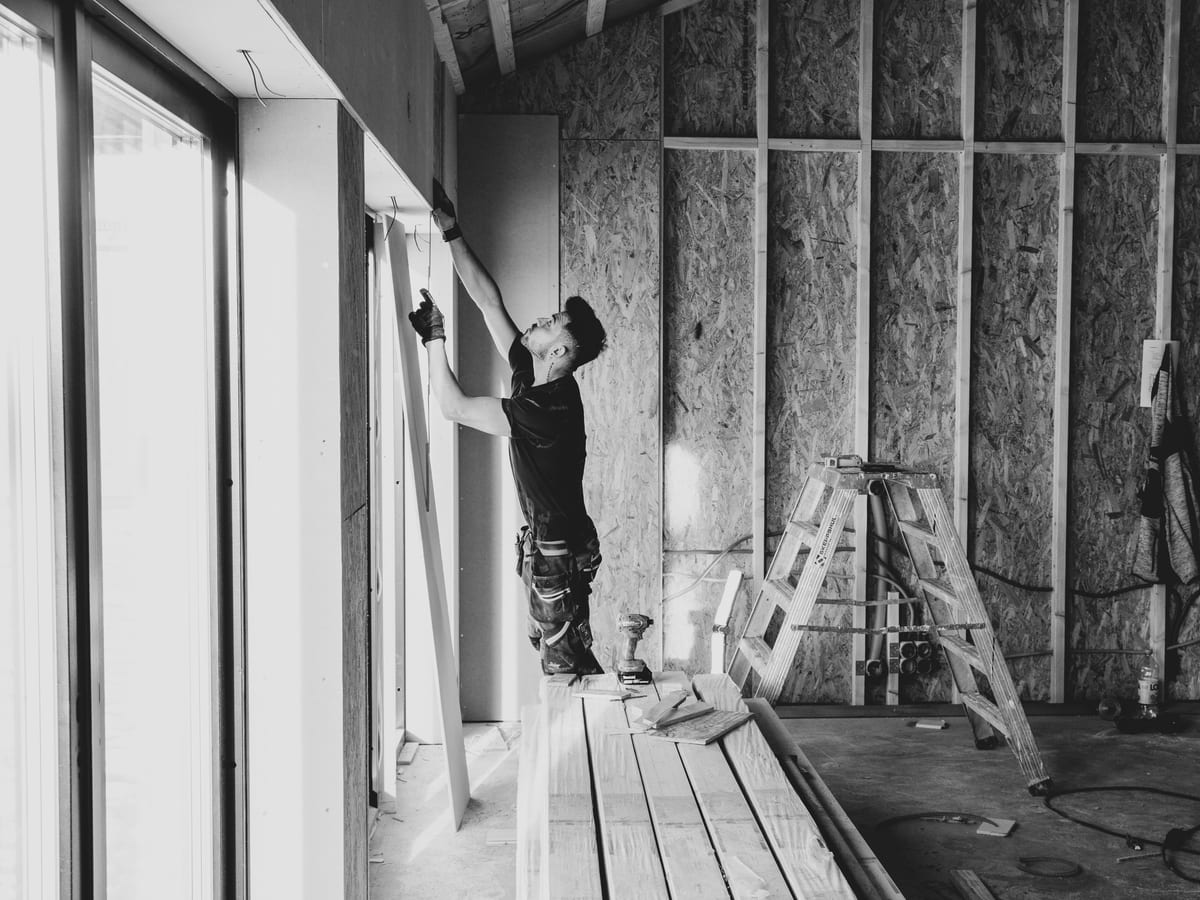 Black and white photo of a worker installing drywall indoors.